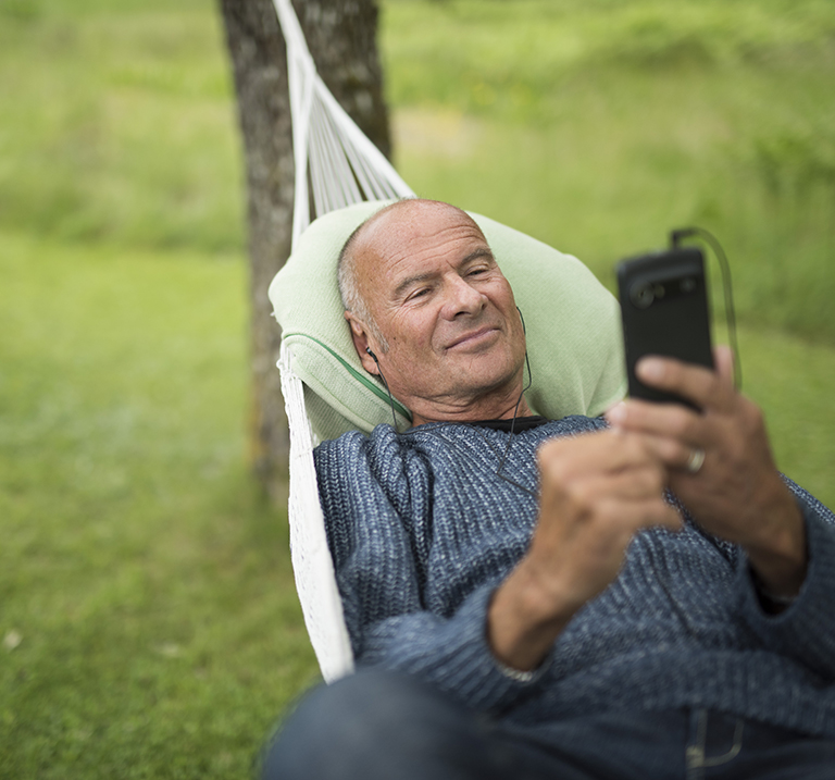 Lasse Holm auf einer Hängematte, mit seinem Doro-Smartphone beschäftigt.
