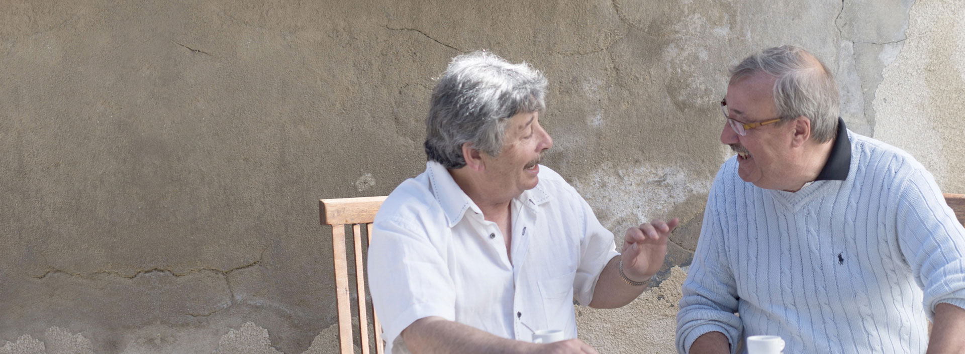Two older men sitting outdoors laughing and talking together