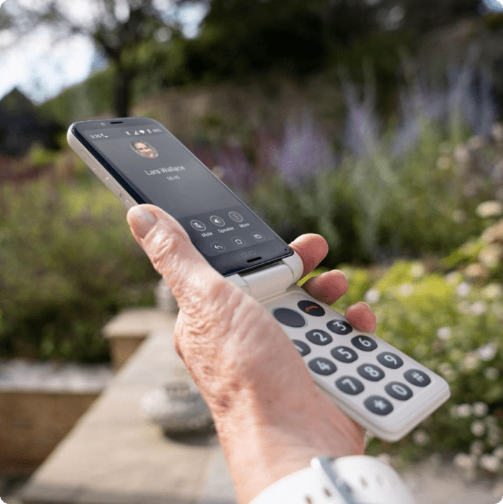 Senior using Doro flip phone with large buttons and clear sound calling feature outdoors