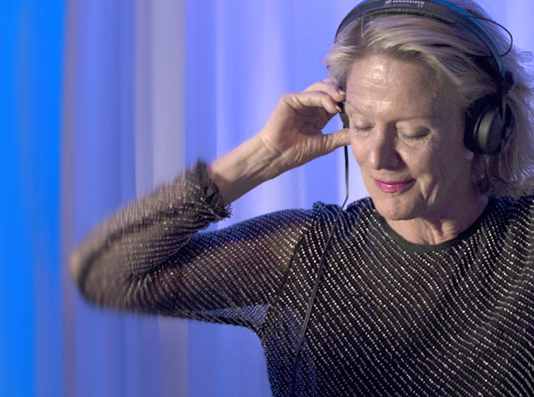 Woman wearing headphones enjoying music with eyes closed against a blue background