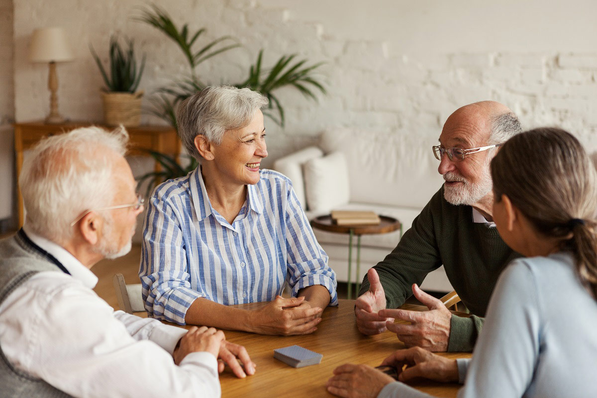 Un groupe de seniors assis ensemble autour d'une table, souriants et discutant amicalement en intérieur.
