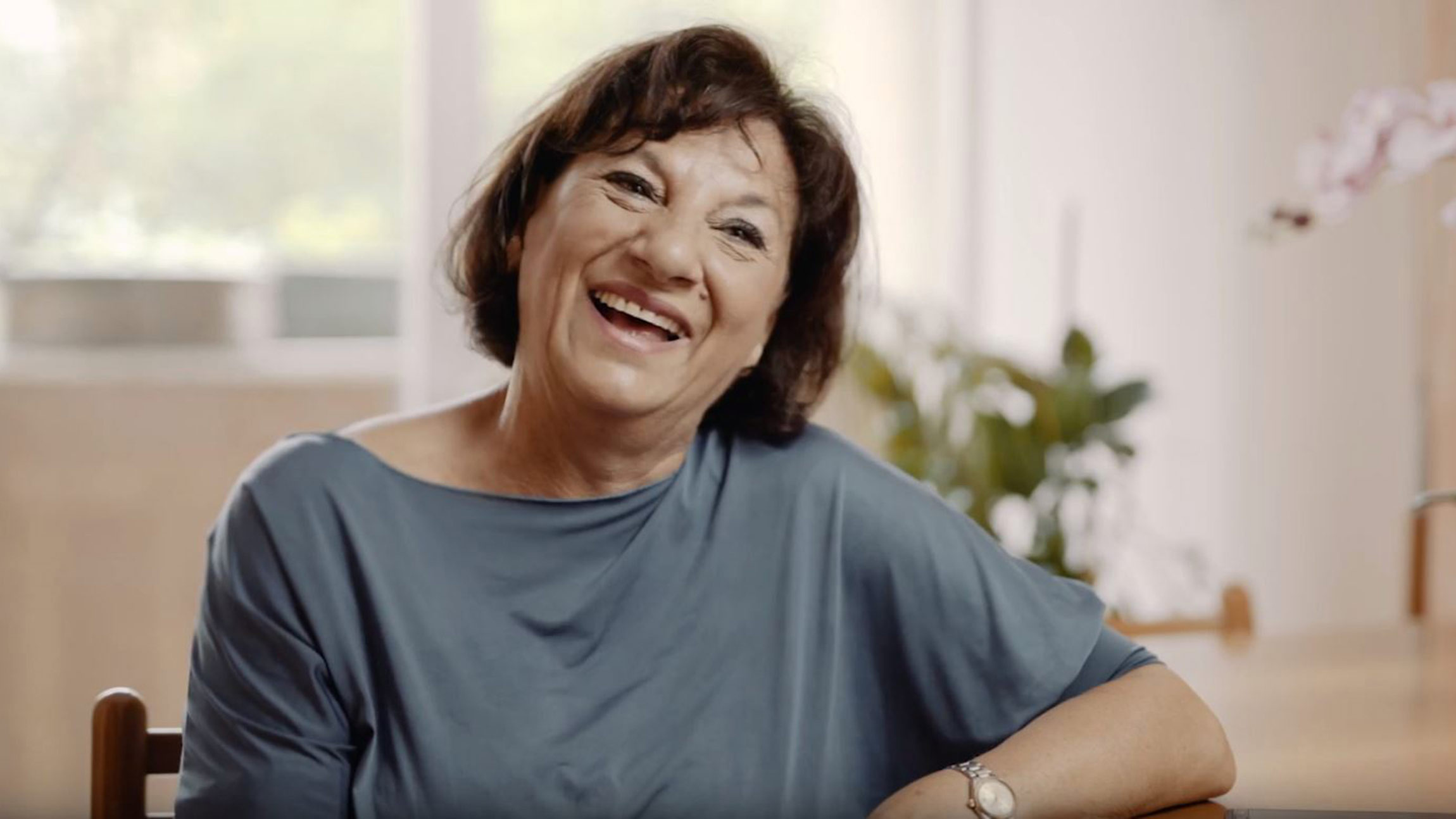 Smiling woman sitting indoors, laughing in a bright and cozy home environment