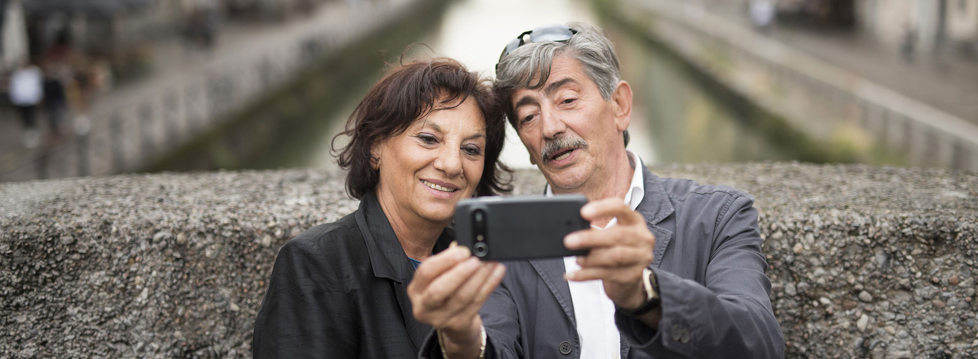 Older couple taking a selfie together with a smartphone while standing by a canal