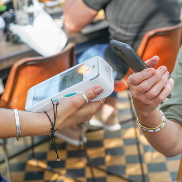 Senior paying with Doro smartphone using contactless mobile payment in café