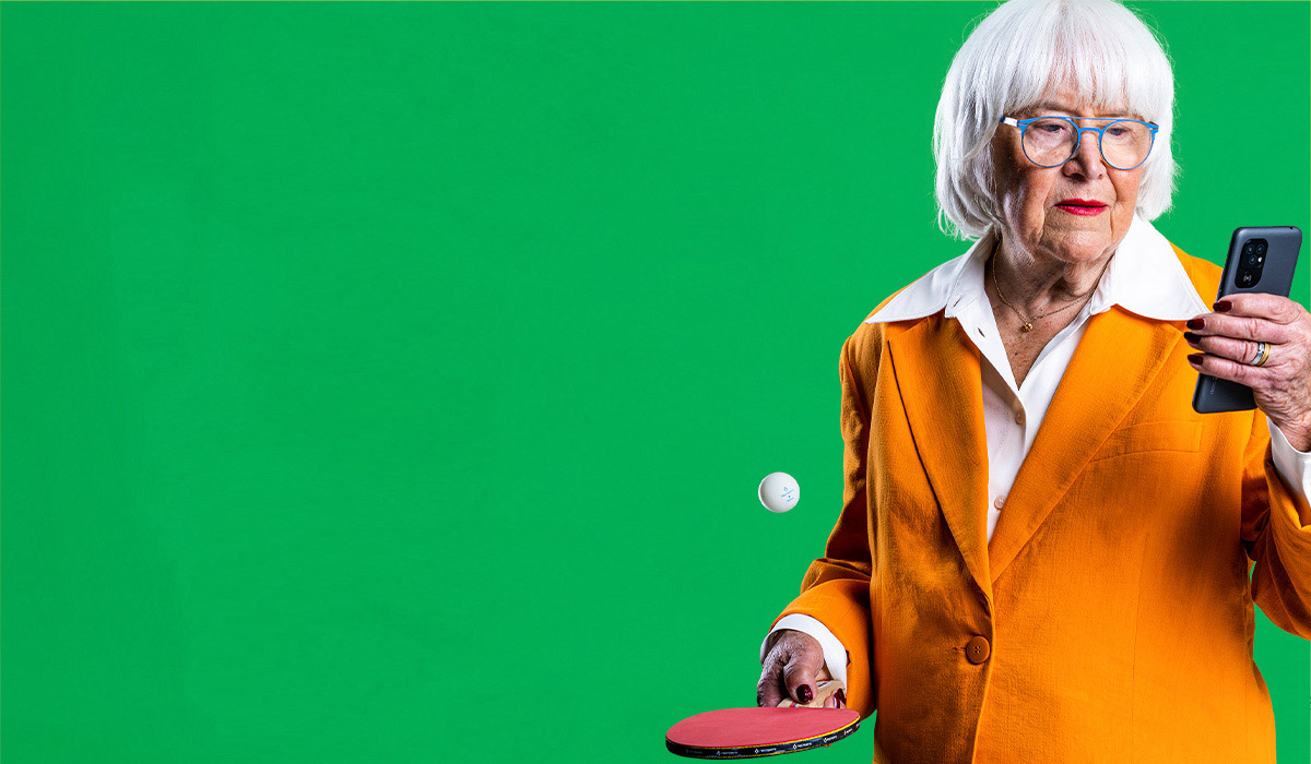 Äldre kvinna i orange blazer använder enkel smartphone för seniorer och visar aktiv livsstil med tennisracket i handen