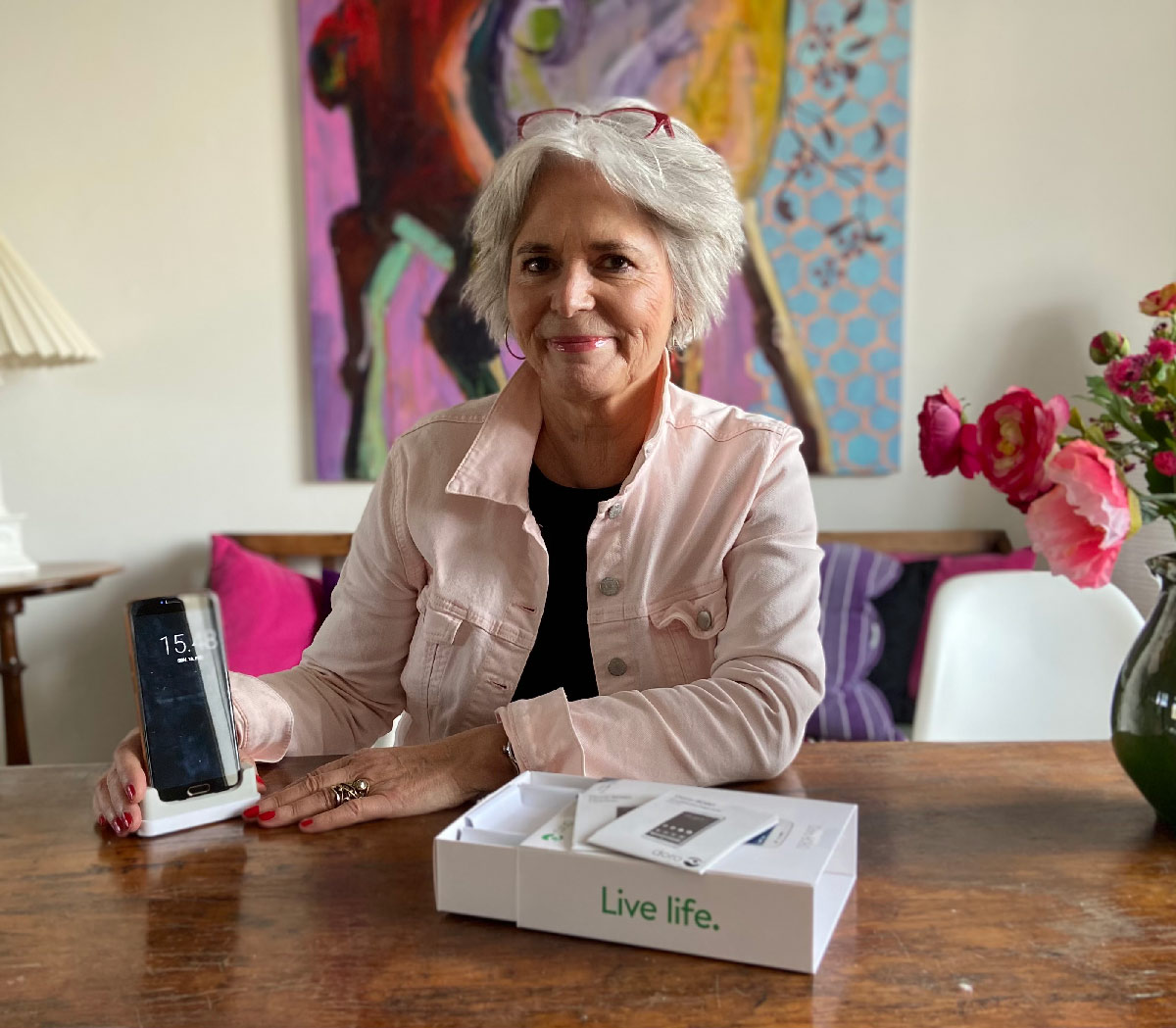 Camilla Lindermann sidder derhjemme og holder en smartphone i en opladningsdock med emballage og tilbehør