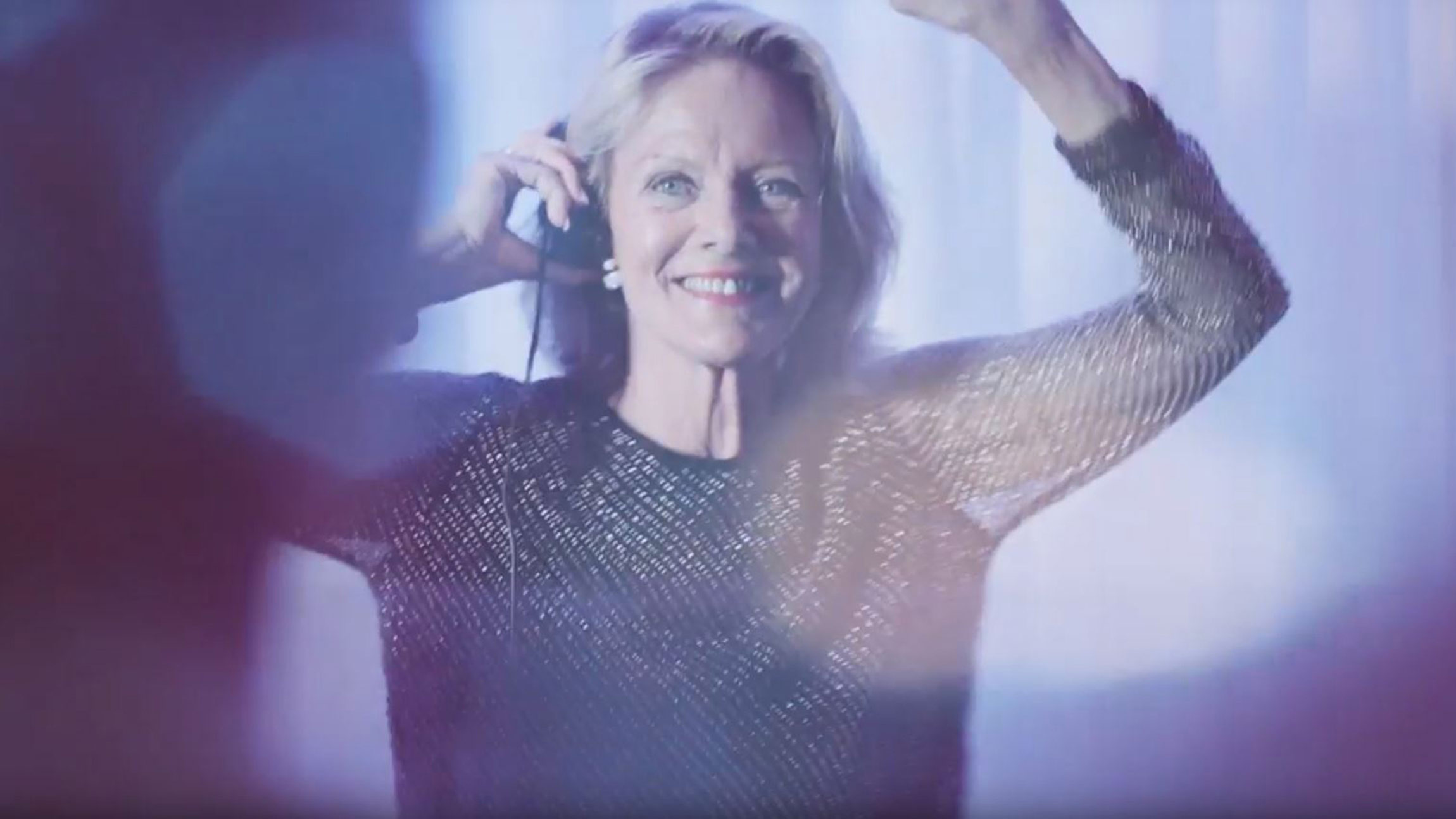 Woman smiling and dancing while listening to music with headphones in a softly lit room
