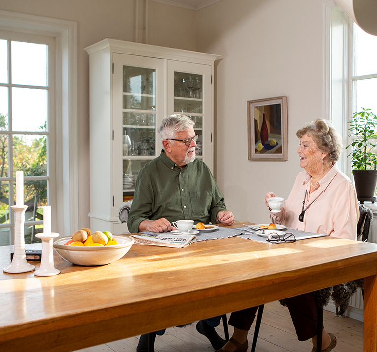two seniors sitting in a kitchen drinking coffee