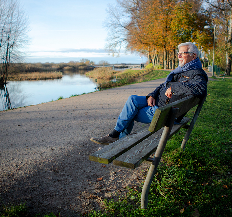 Äldre man sitter på en bänk vid en flod